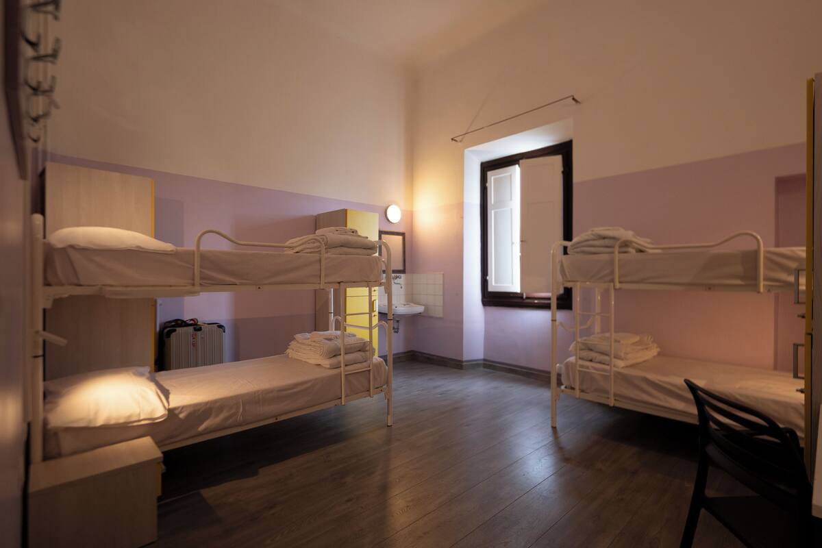 A dormitory room with bunk beds, a sink, and a window.