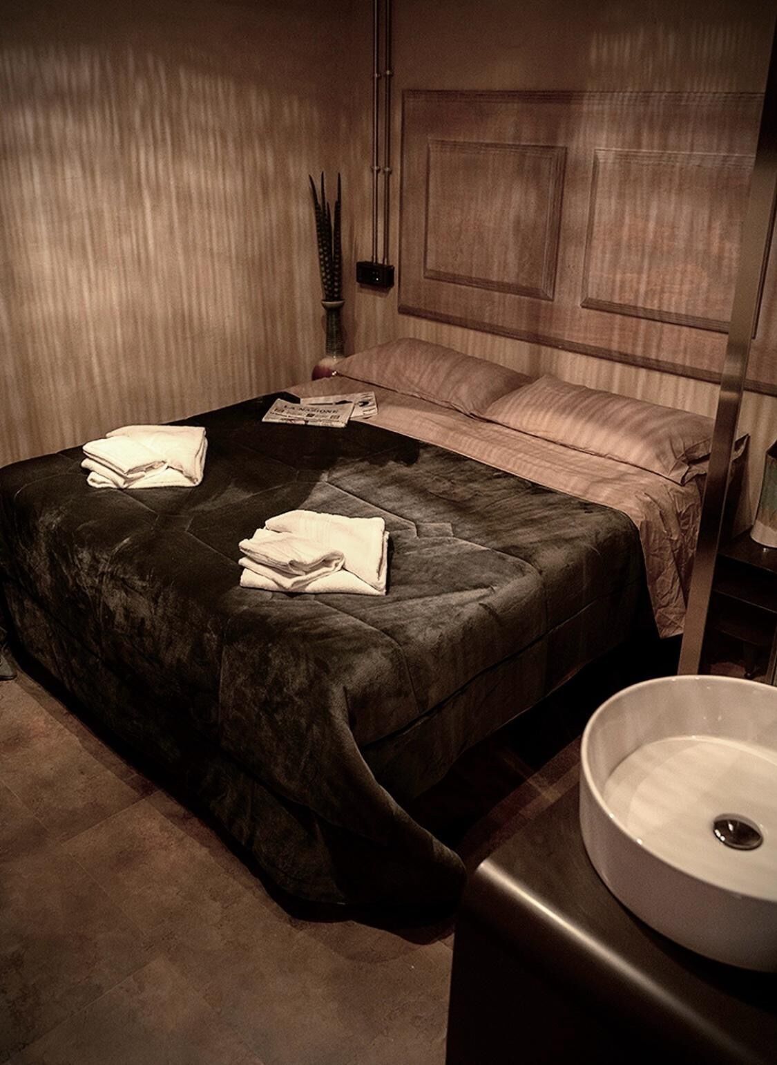 A hotel room with a large bed, a bedside table, and a round sink.