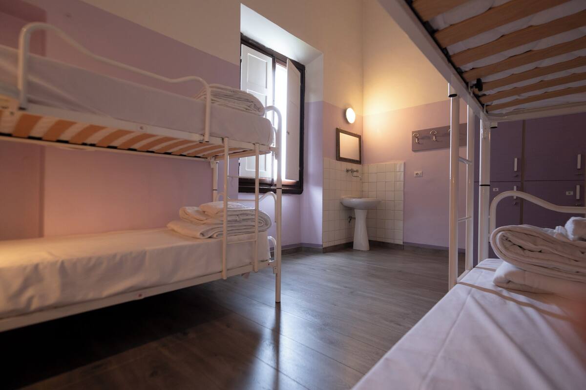 A dormitory room with bunk beds, a sink, and a window.