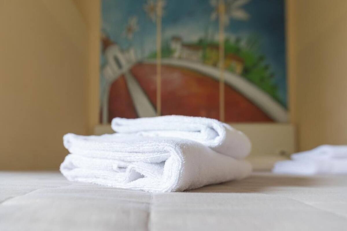 A neatly folded white towel on a white surface with a painting in the background.