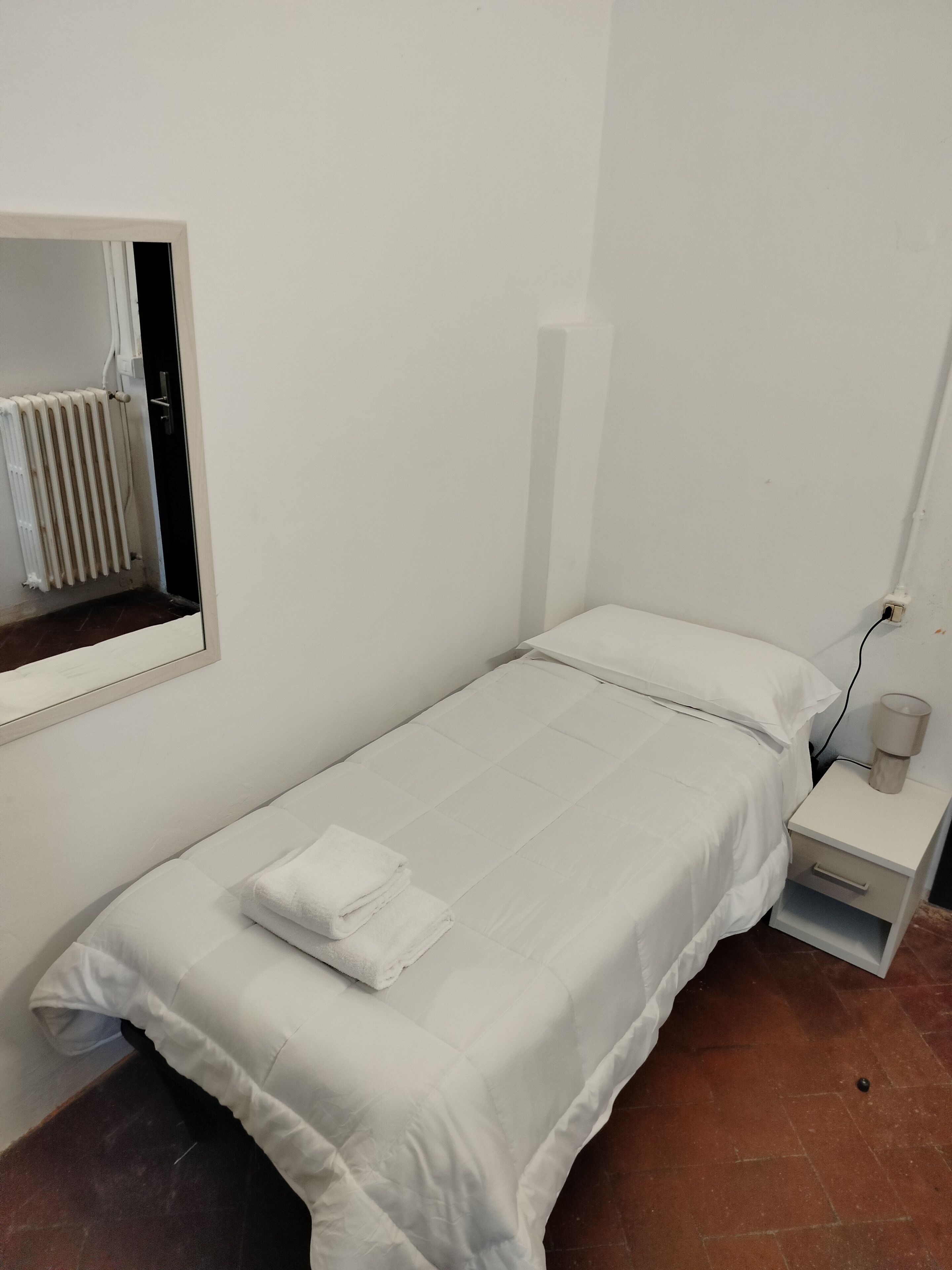 Une petite chambre propre, avec un lit simple, une table de chevet avec une lampe et un radiateur.
