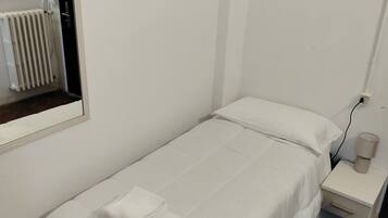 Une petite chambre propre, avec un lit simple, une table de chevet avec une lampe et un radiateur.