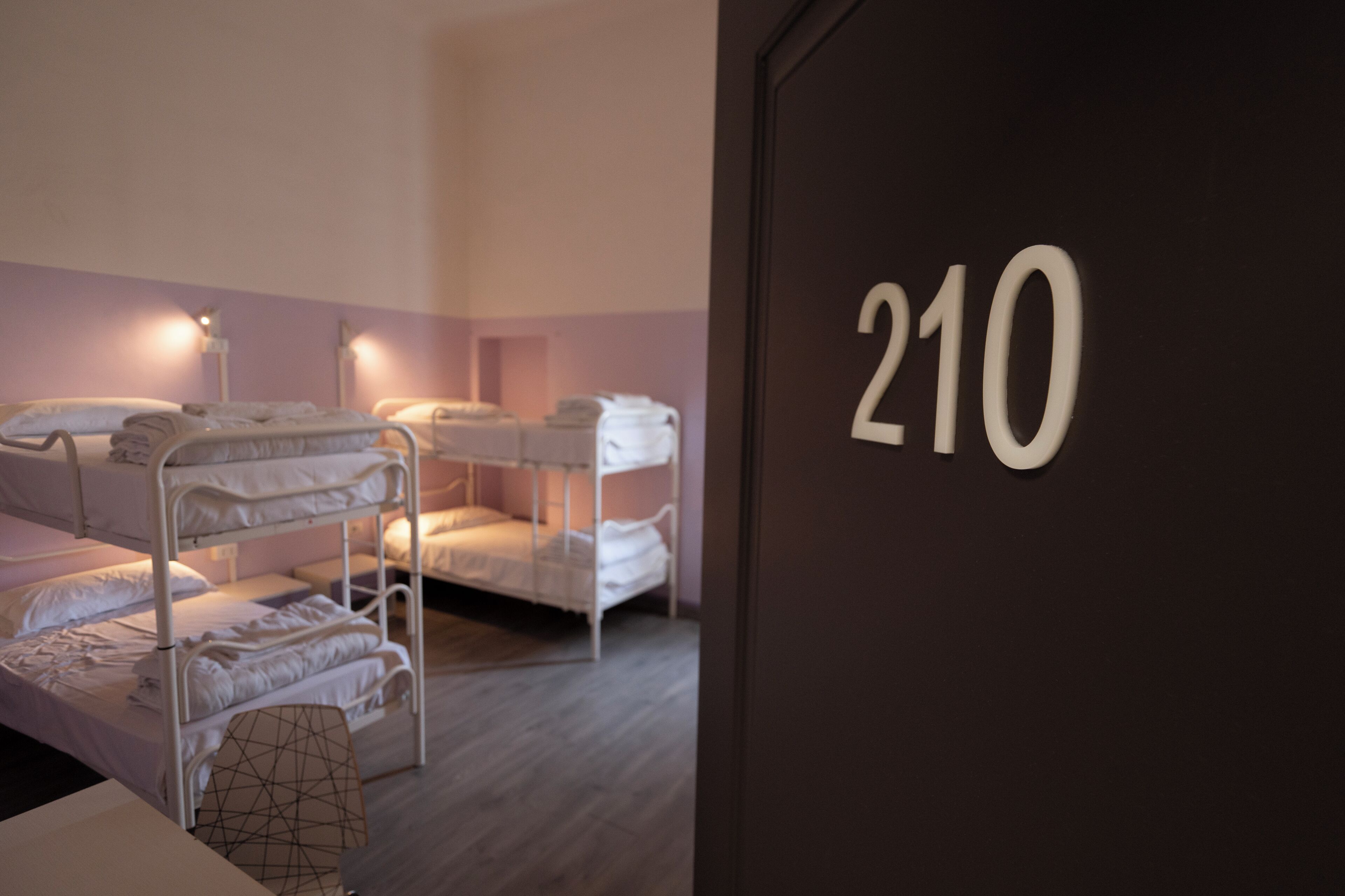 Une chambre avec des lits superposés, le numéro « 210 » écrit sur le mur et un coussin à motifs géométriques posé sur le sol.