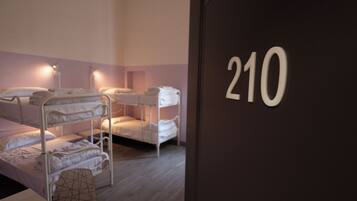 Une chambre avec des lits superposés, le numéro « 210 » écrit sur le mur et un coussin à motifs géométriques posé sur le sol.