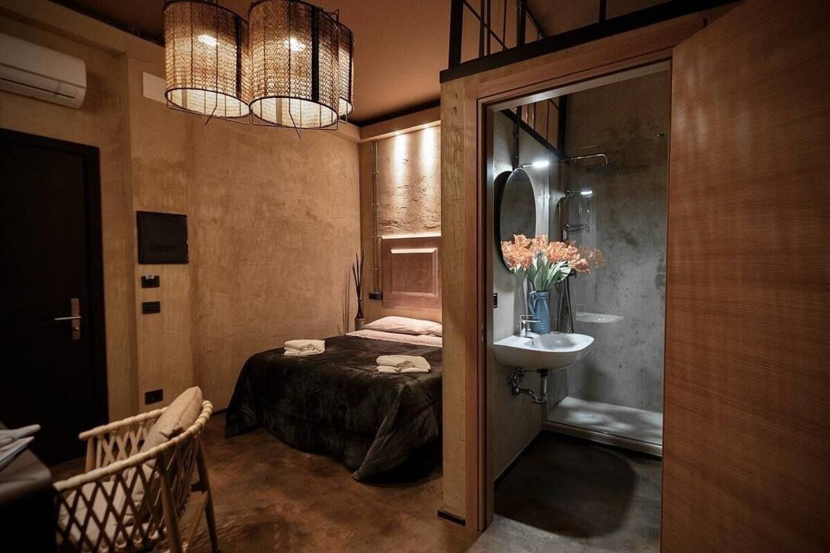 A compact bedroom with a bed, a chair, and a bathroom with a sink and shower.