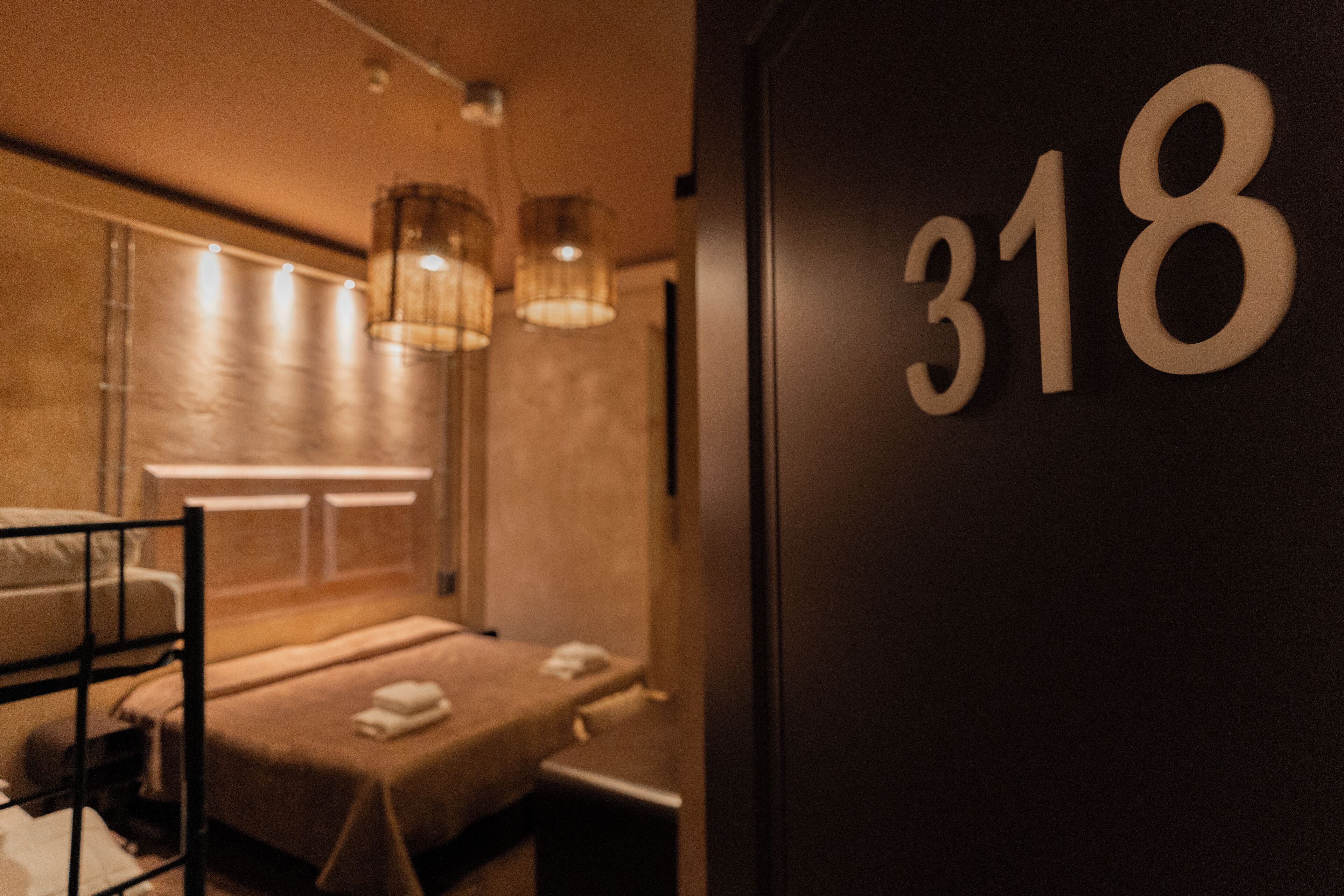 Habitació d'hotel amb un llit superposat, una taula de nit i el número '318' penjat a la paret.