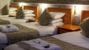 A hotel room with three beds, each with a wooden headboard and patterned bedding. There are bedside tables with lamps and a wall-mounted light fixture. - The Grainger Hotel (Newcastle-upon-Tyne)