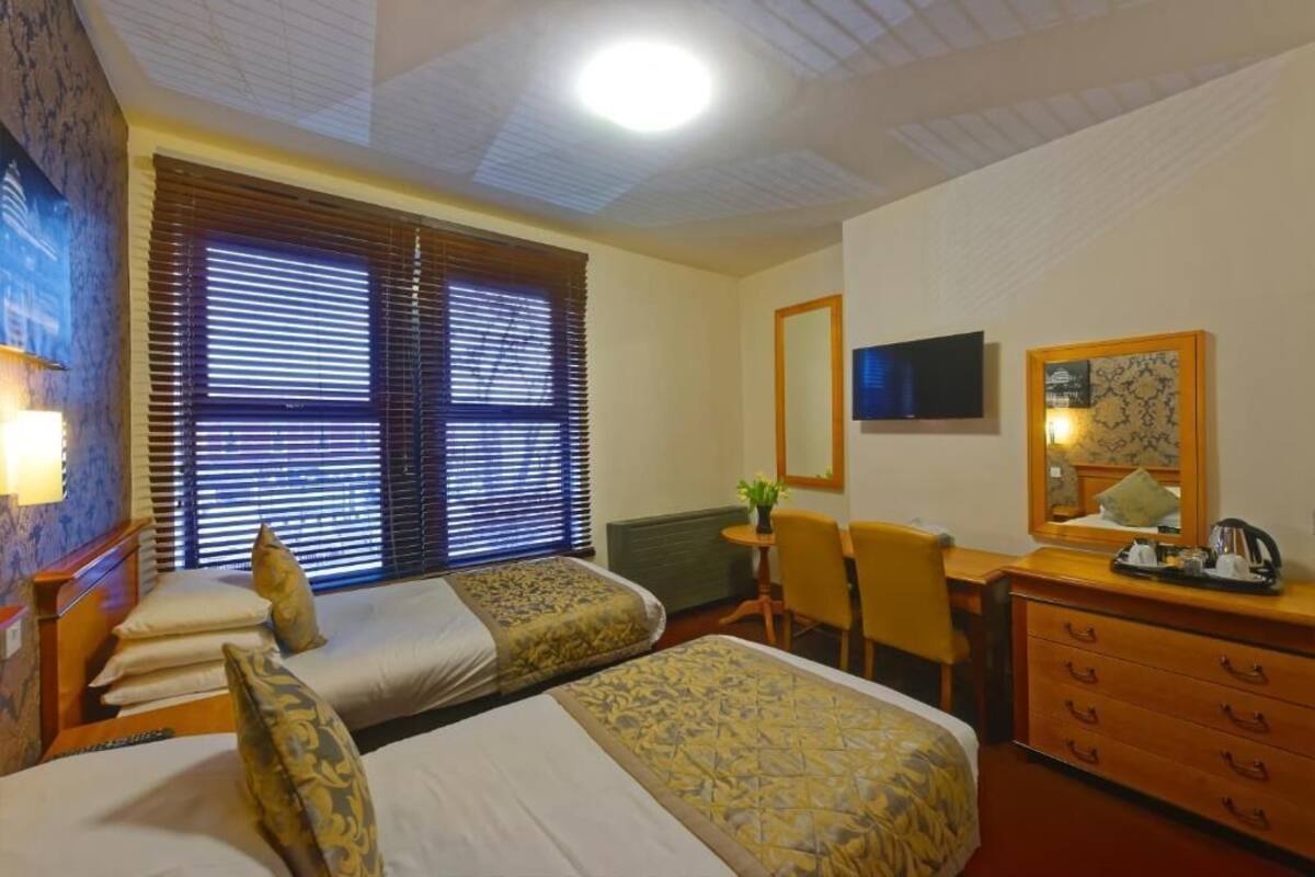 Une chambre d’hôtel avec deux lits, un bureau, une chaise, une commode et un téléviseur.