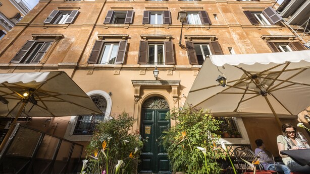 A building with multiple windows and a green door, surrounded by outdoor seating areas with umbrellas. - Casa de' Fiori Biscione (Rome)