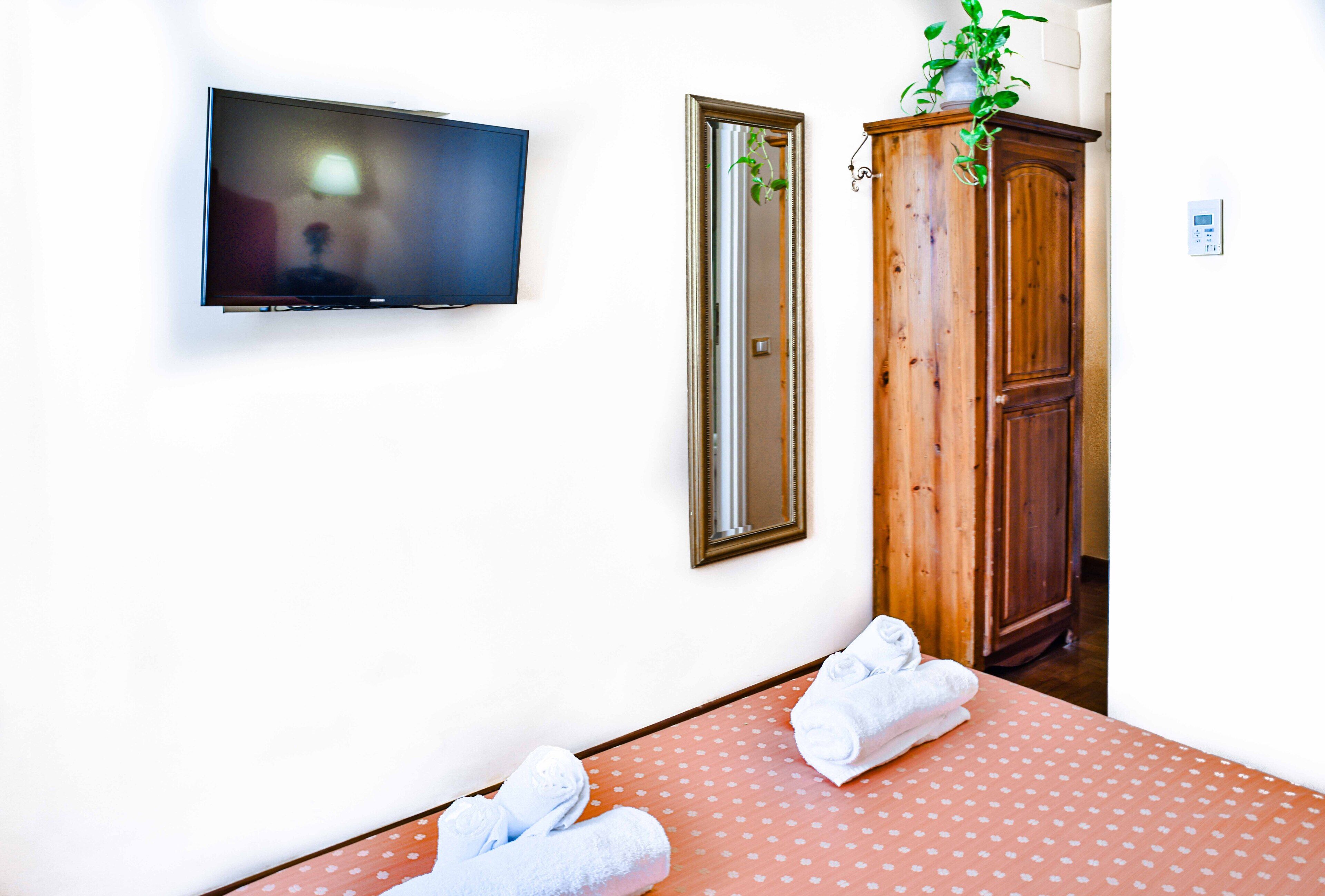 Una habitación con un televisor montado en la pared, un espejo, un armario de madera y una cama con edredón estampado de lunares.