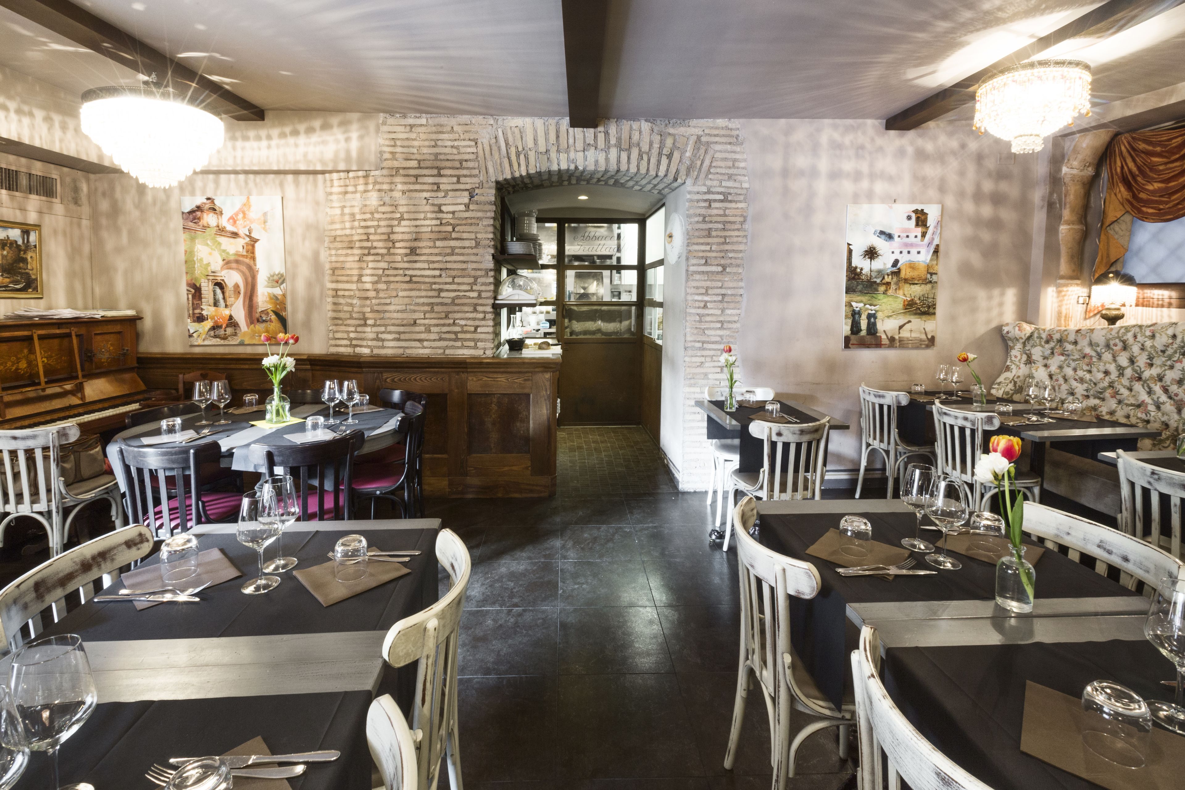 A restaurant with brick walls, wooden furniture, and chandeliers. Tables are set with wine glasses and cutlery.