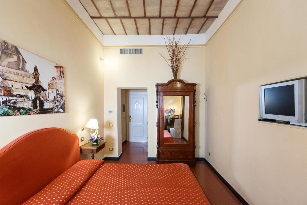 A hotel room with a bed, a wooden dresser, a mirror, a television, and a painting on the wall.