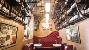 A restaurant interior with a red upholstered bench, tables with vases, and wine bottles on shelves. - Casa de' Fiori Biscione (Rome)