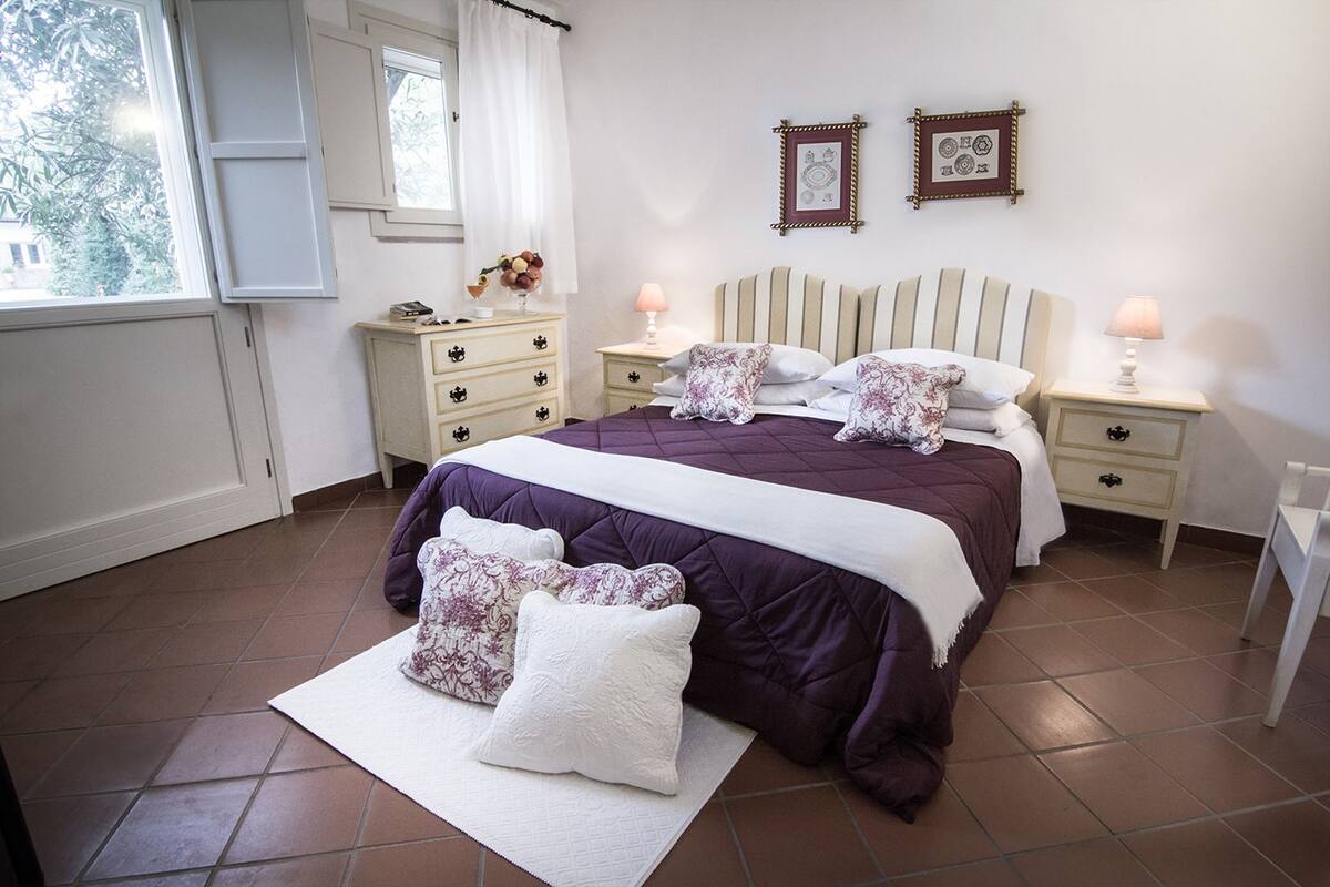 A bedroom with a large bed, two bedside tables, a nightstand, a dresser, and a window with curtains.