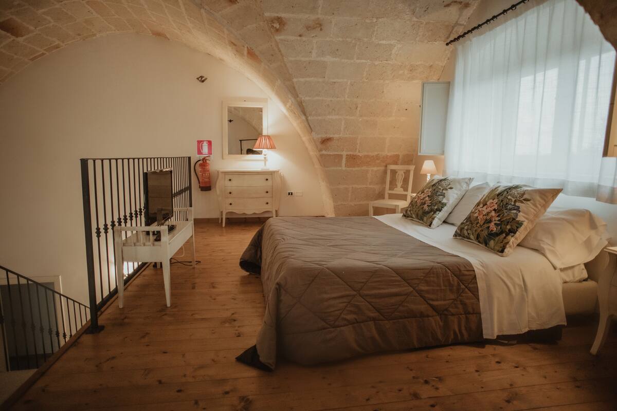 A bedroom with a wooden floor, a bed with floral pillows, a dresser, and a mirror.