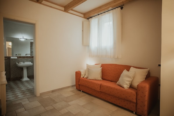 A room with a sofa, a window with curtains, a sink, and a tiled floor.