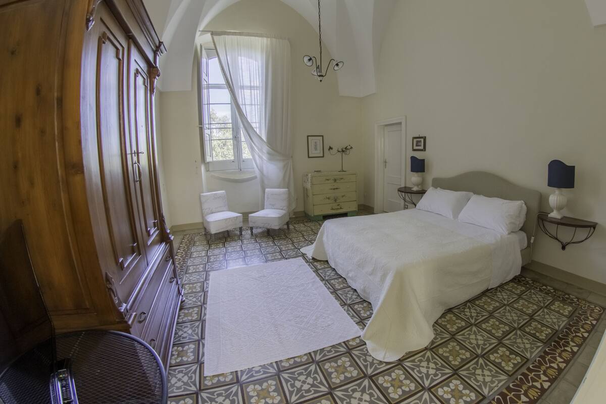 A bedroom with a large bed, a wooden wardrobe, a desk, and a chair.