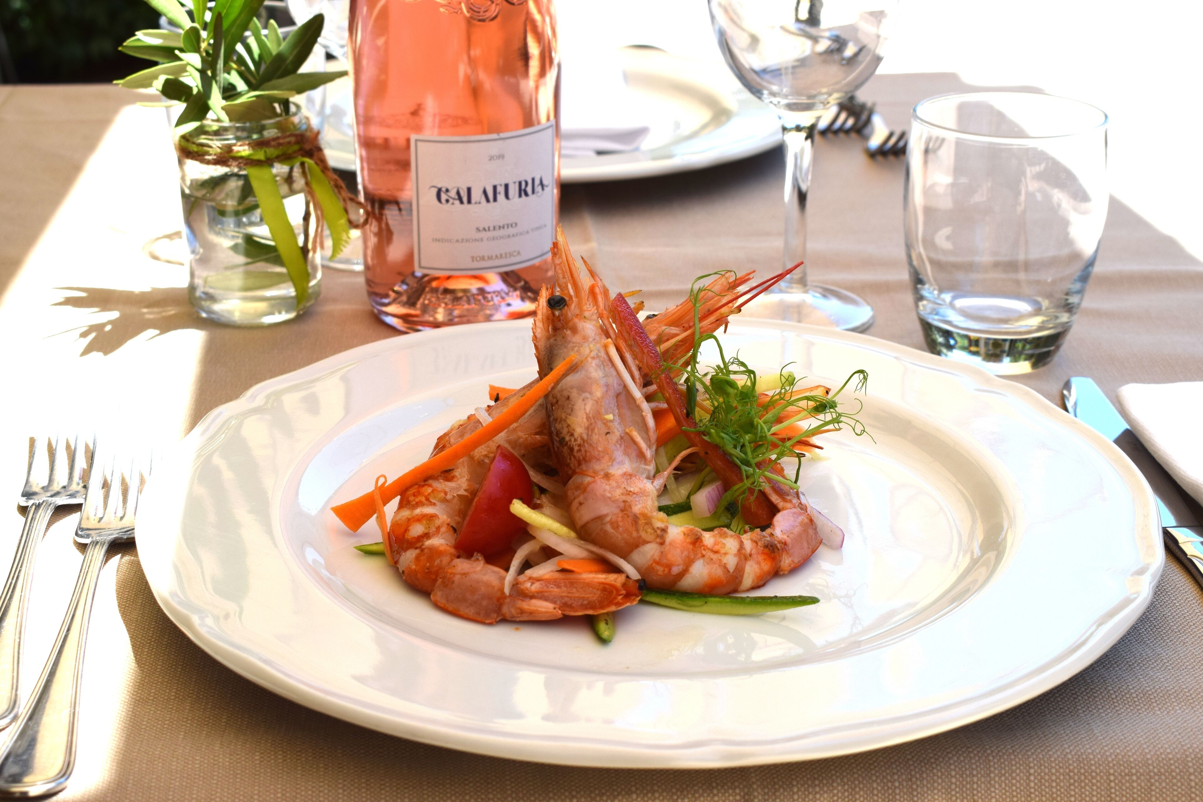 A plate of food with a shrimp centerpiece, a bottle of wine, and a glass of water on a table.