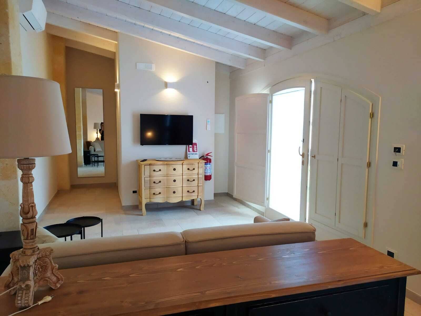 A living room with a wooden table, a TV mounted on the wall, a sofa, and a cabinet.