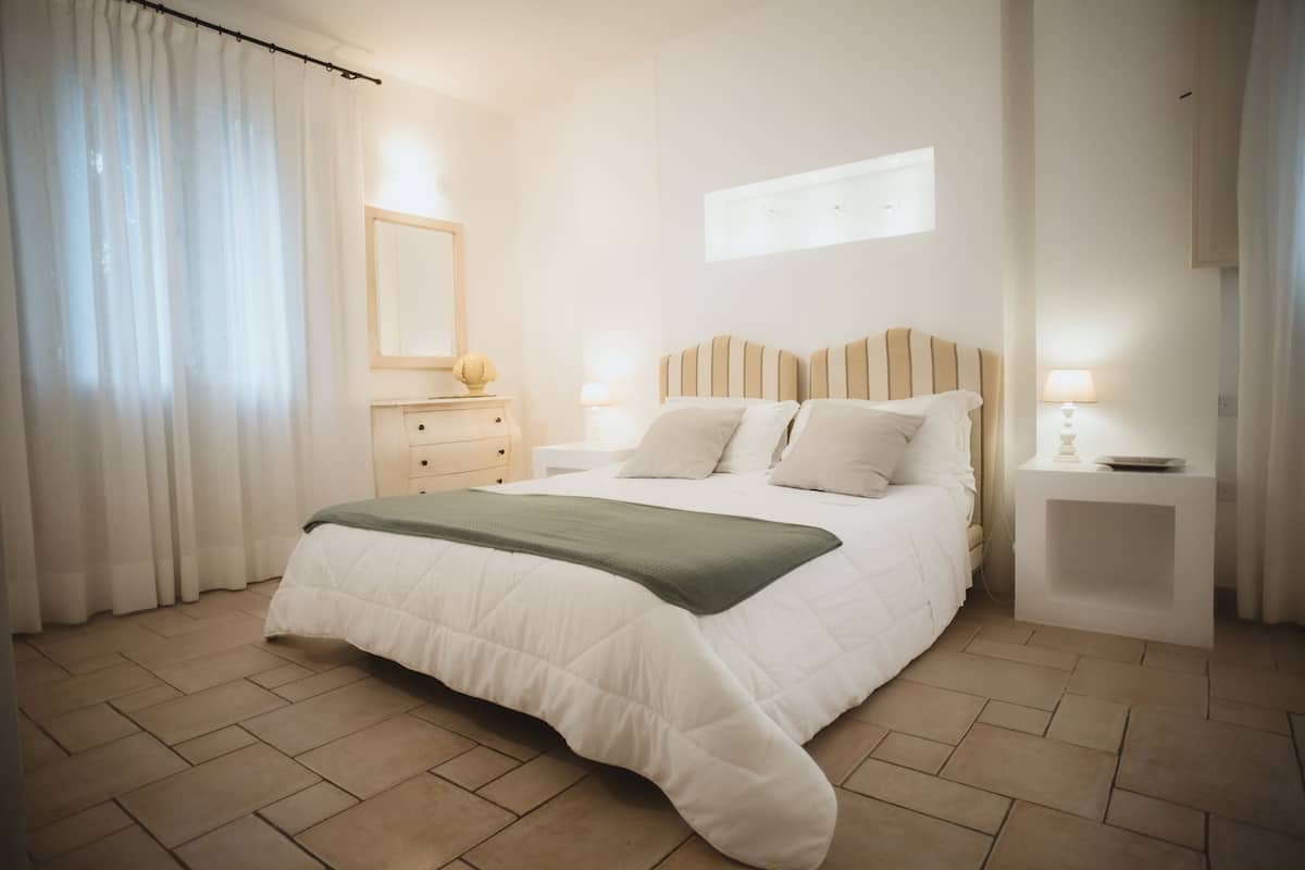 A bedroom with a bed, bedside tables, a nightstand, a mirror, and a window with curtains.