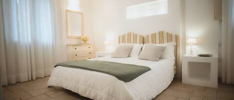 Une chambre à coucher avec un lit, des tables de chevet, une commode, un miroir et une fenêtre avec des rideaux.
