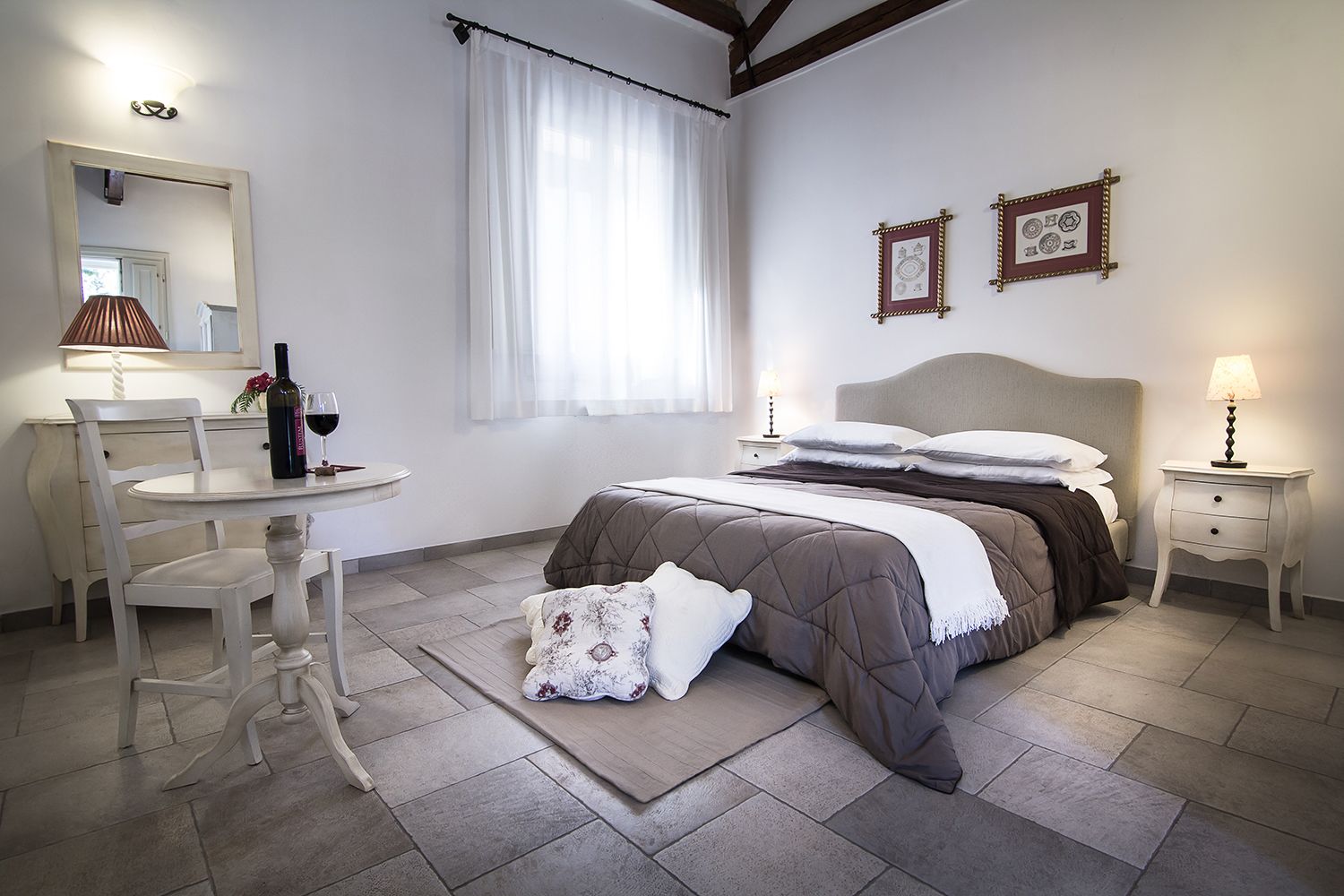 Un dormitorio con cama, mesitas de noche, una silla, un escritorio y una ventana con cortinas.