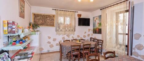 A dining area with a table and chairs, a shelf with food items, and a painting on the wall.