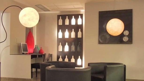 Un espace d’accueil moderne comprenant un comptoir, des chaises, un panneau décoratif mural et un grand luminaire circulaire.