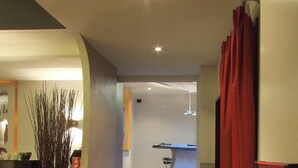 Un couloir d’hôtel moderne avec un mur incurvé, un rideau rouge et un bar visible au fond.