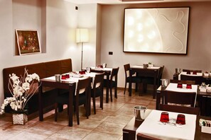 A restaurant with multiple tables and chairs, a decorative plant, and a wall-mounted light fixture. - Re Di Roma Hotel (Rome)