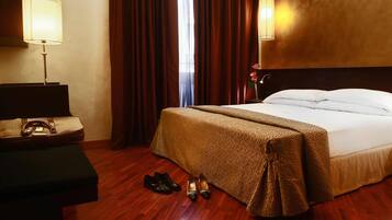 Une chambre d’hôtel avec un lit, un bureau doté d’une lampe, un vase avec des fleurs et une paire de chaussures posées sur le sol.