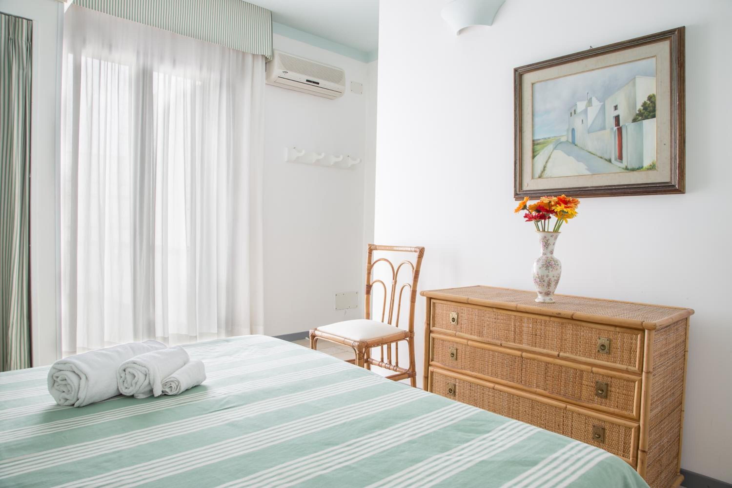 Una camera d'albergo con un letto, una sedia, una cassettiera e un quadro appeso al muro.