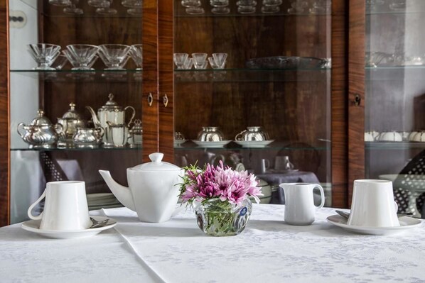 A dining area with a white table set for tea service, a cabinet with glassware, and a vase with flowers. - Palazzo Angelelli (Gallipoli)