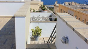 A rooftop terrace with potted plants, a metal railing, and a view of the sea. - Palazzo Angelelli (Gallipoli)
