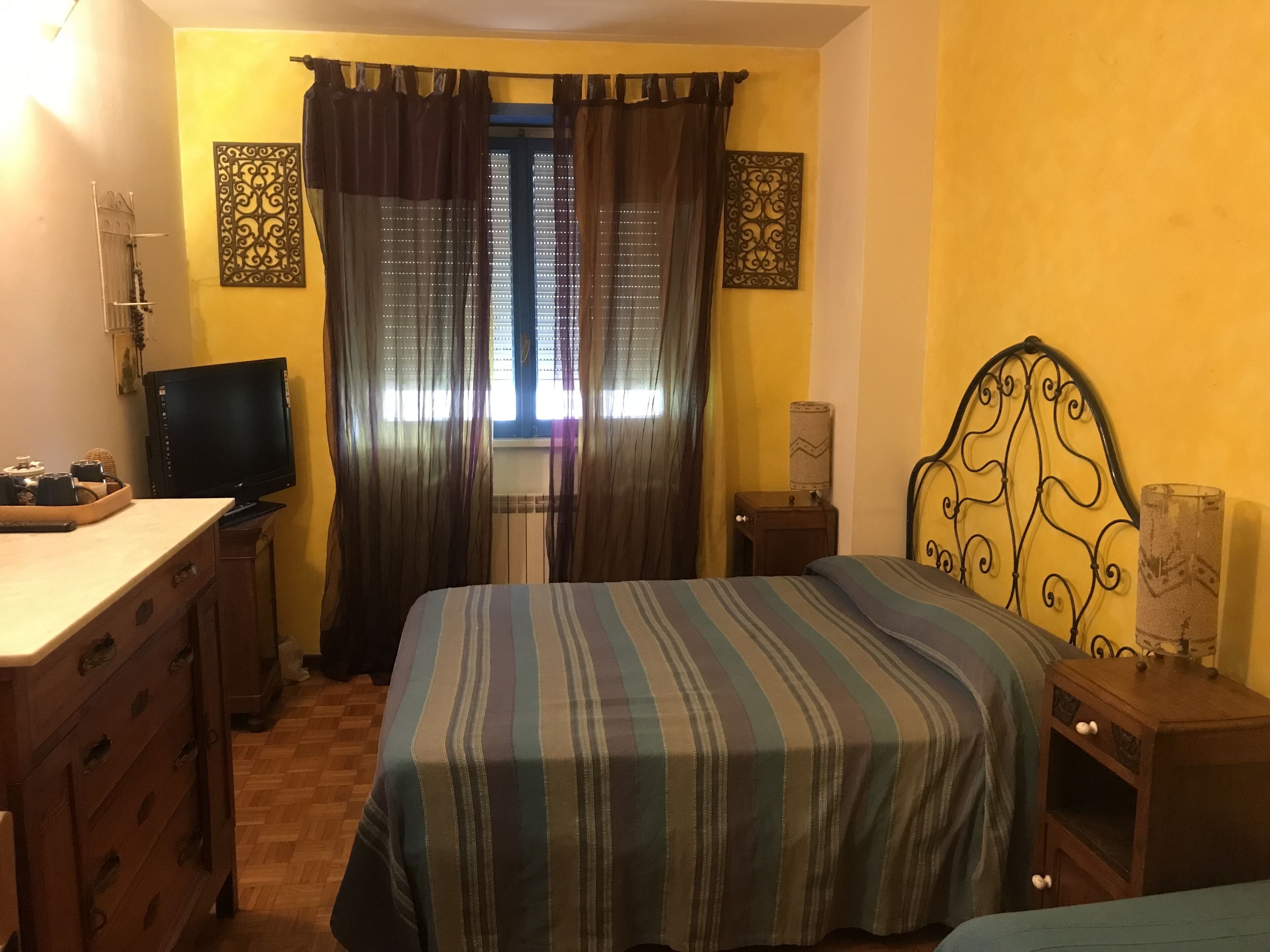 A bedroom with a bed, a television, a desk, and a window with curtains.
