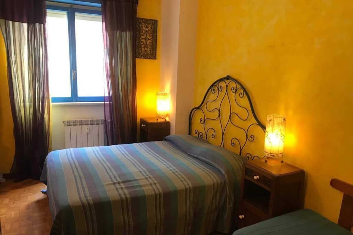 Un dormitorio con dos camas, una ventana con cortinas, un radiador y lámparas de noche.