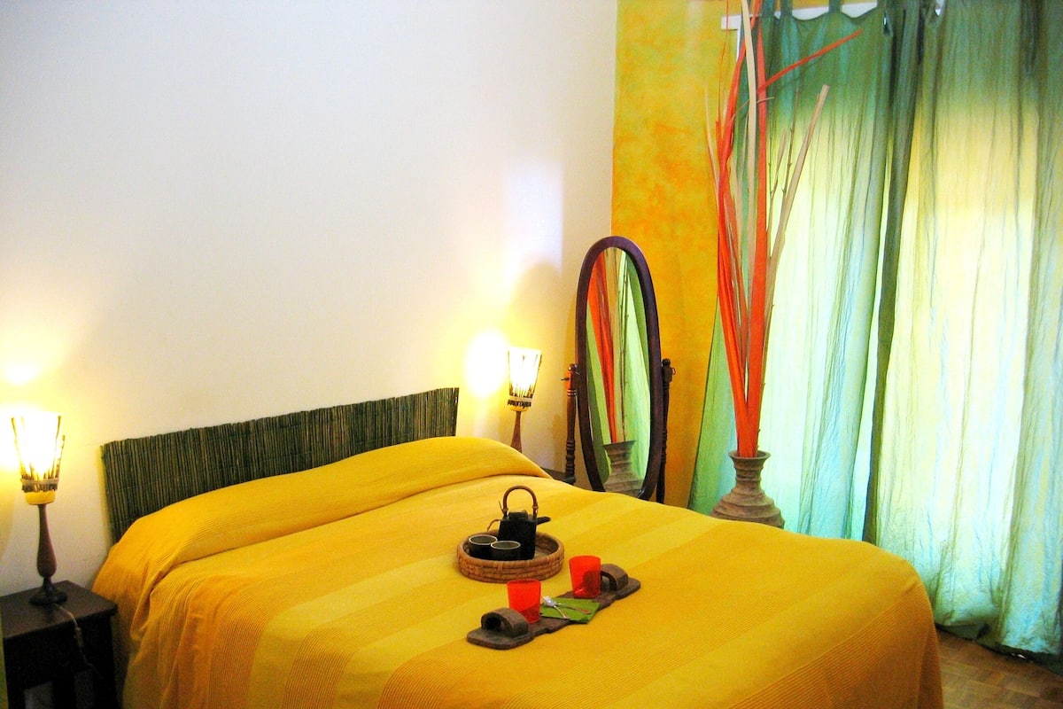 Una habitación de hotel con cama, lámparas de noche, un espejo y una ventana con cortinas.