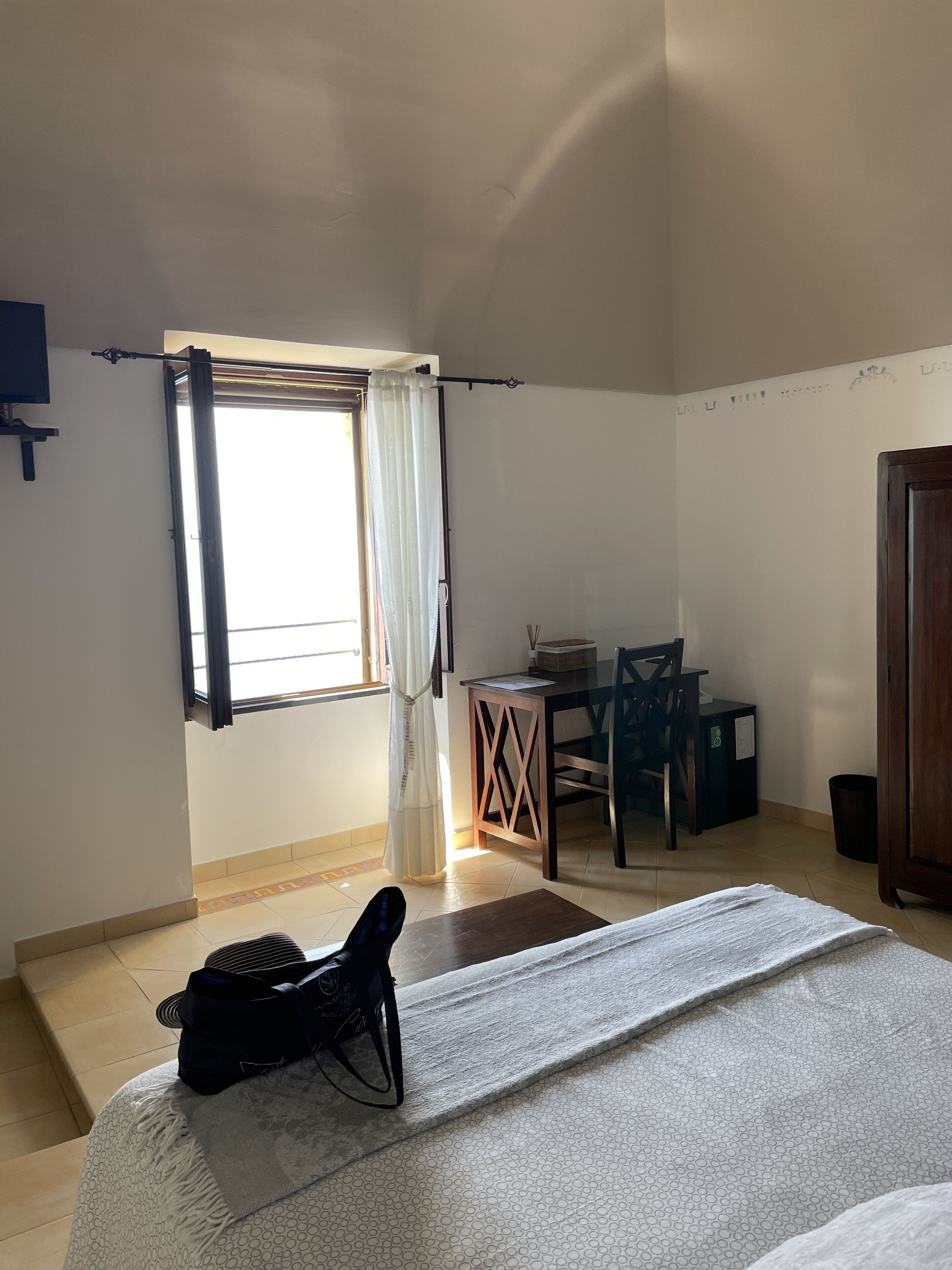 Una habitación con cama, escritorio, silla y ventana con cortinas.