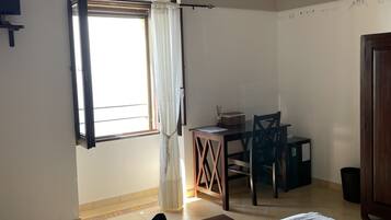 Una habitación con cama, escritorio, silla y ventana con cortinas.