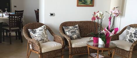 A living room with wicker furniture, a dining area with chairs, a table with a vase, and a decorative rug.