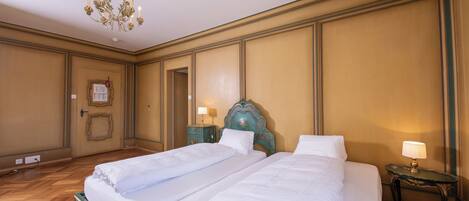 Ein Hotelzimmer mit zwei Betten, einer Kandelaber, einem kleinen Tisch mit Lampe und einem gerahmten Bild an der Wand.