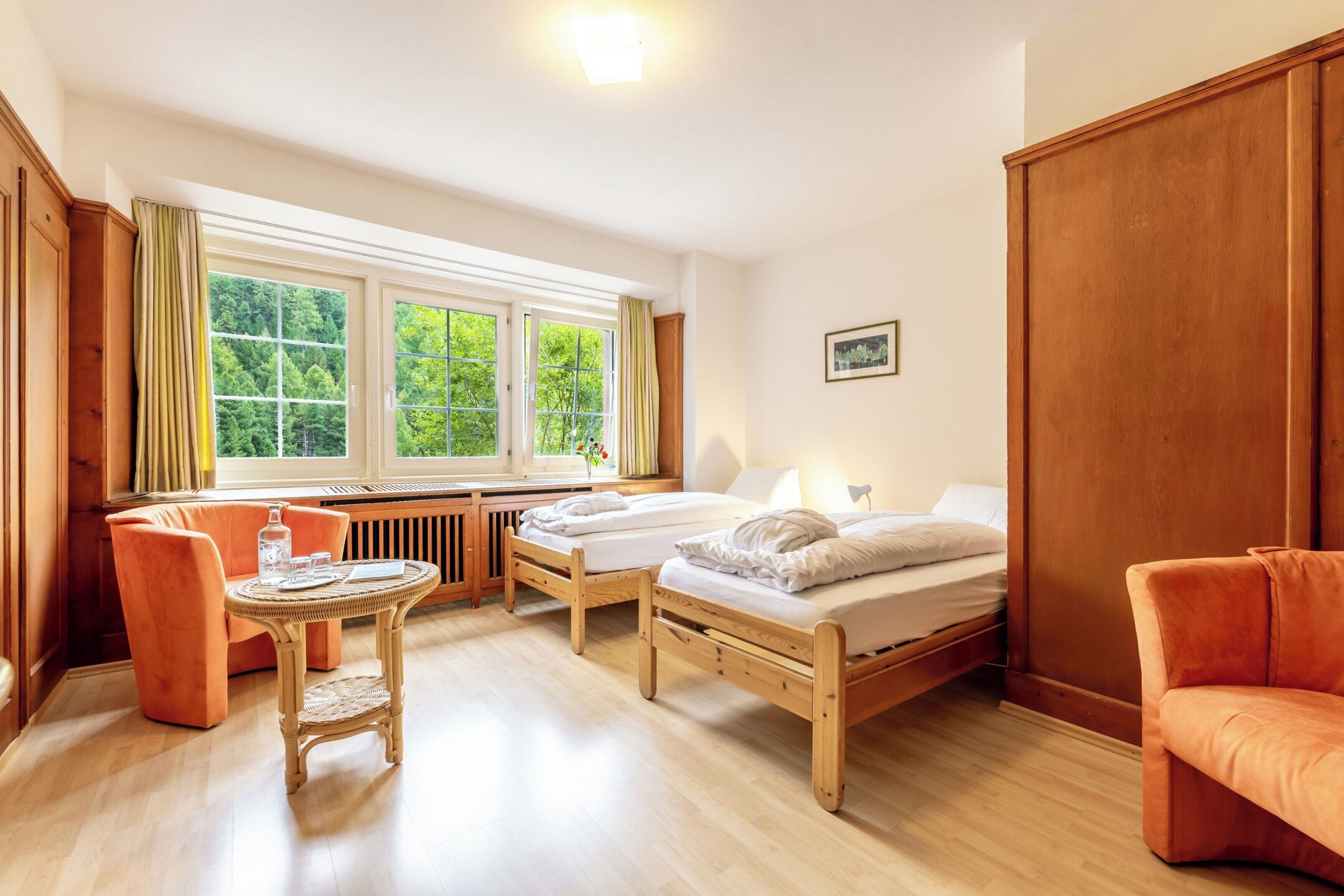 Ein Zimmer mit zwei Holzbetten, einem Korbstuhl und einem orangefarbenen Sofa.