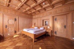 Un dormitorio con paneles de madera, una cama grande, dos mesitas de noche y un techo con vigas de madera.