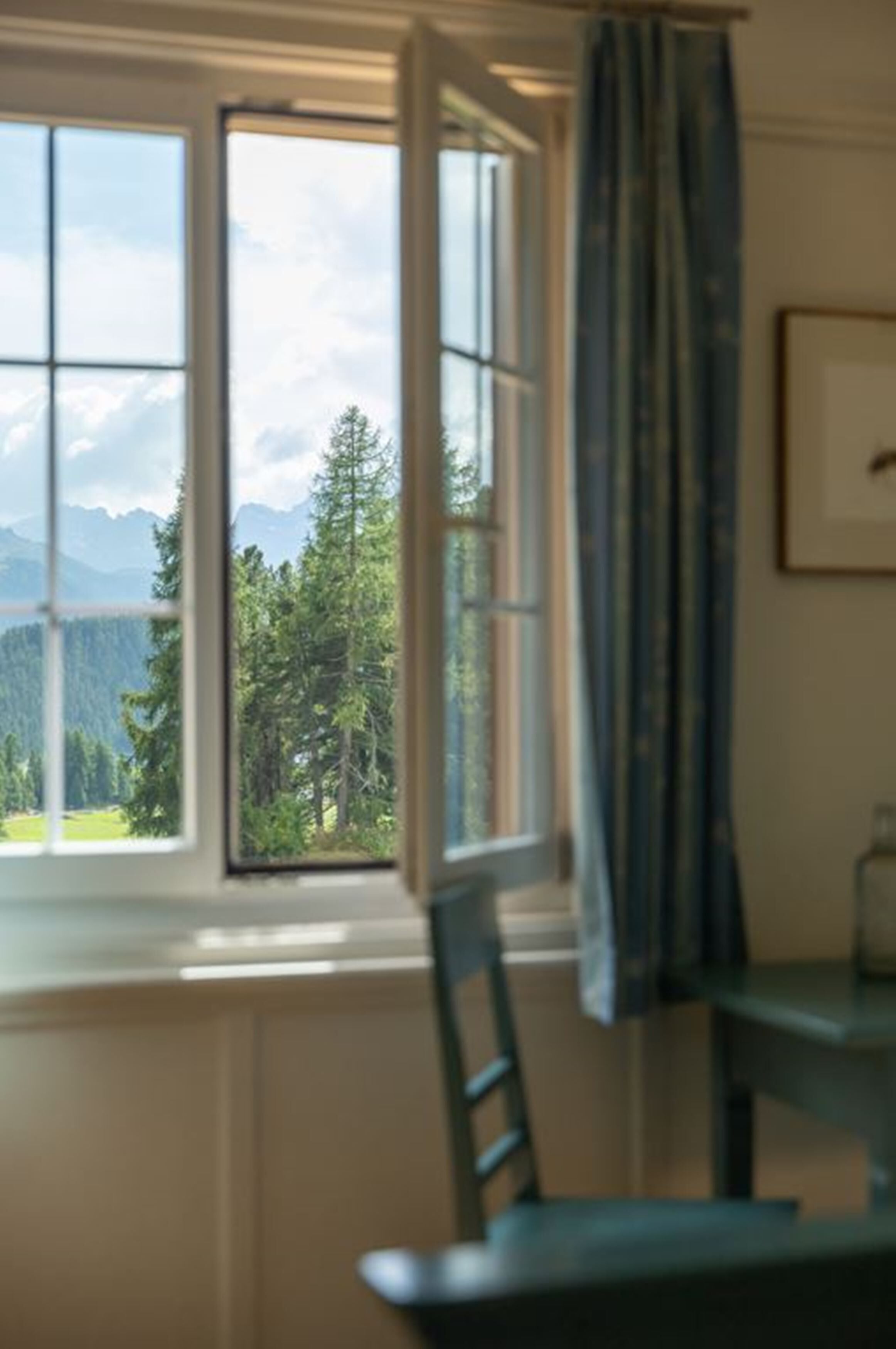 Una habitación con un amplio ventanal que ofrece vistas a un bosque y montañas.