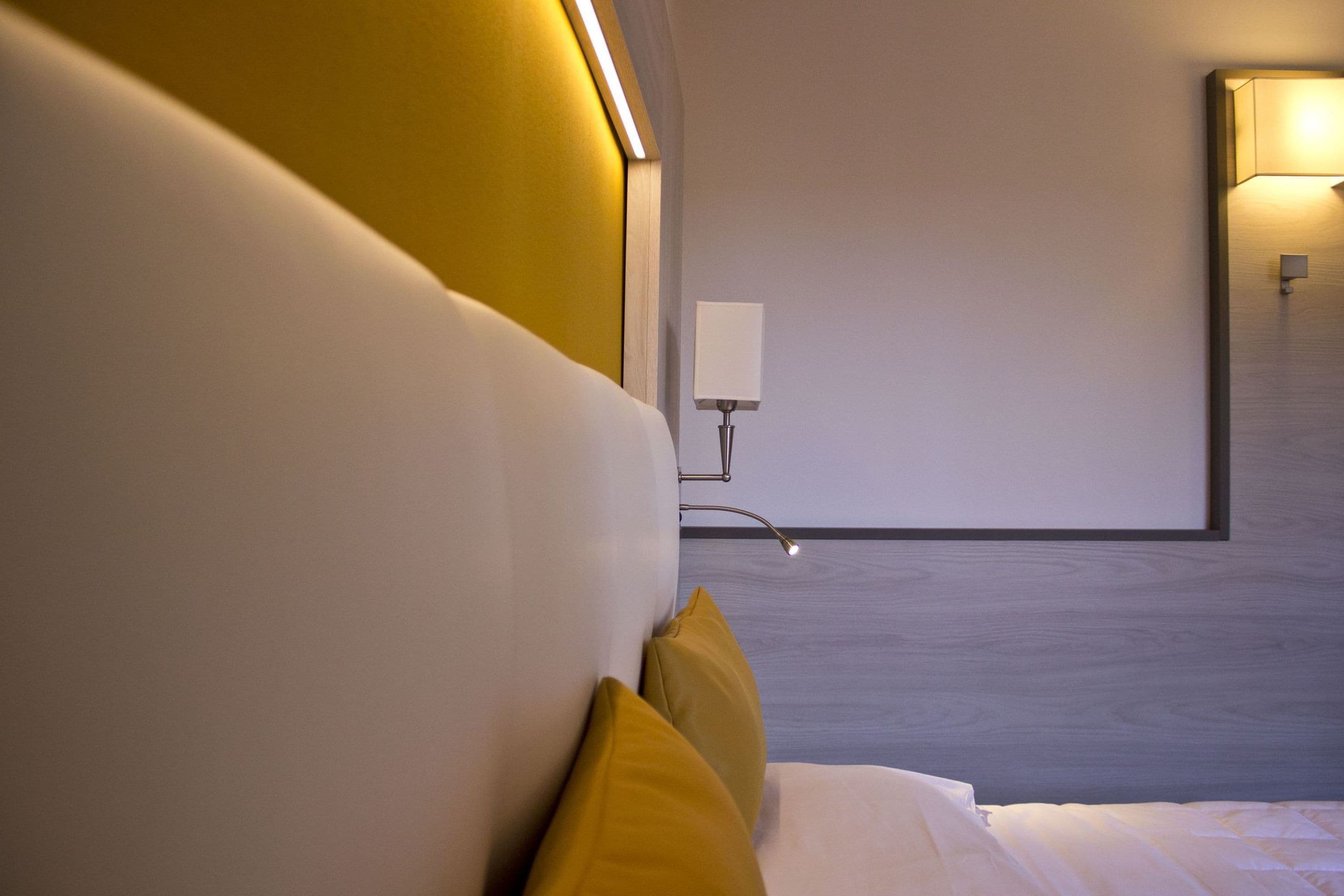 A modern hotel room with a large bed, a bedside table, and a wall-mounted lamp.