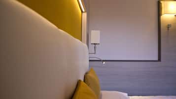 A modern hotel room with a large bed, a bedside table, and a wall-mounted lamp.