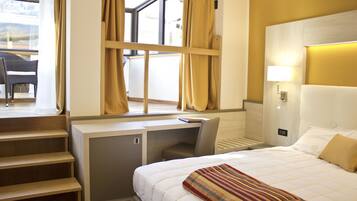 A hotel room with a bed, desk, chair, and a view of the outdoors.