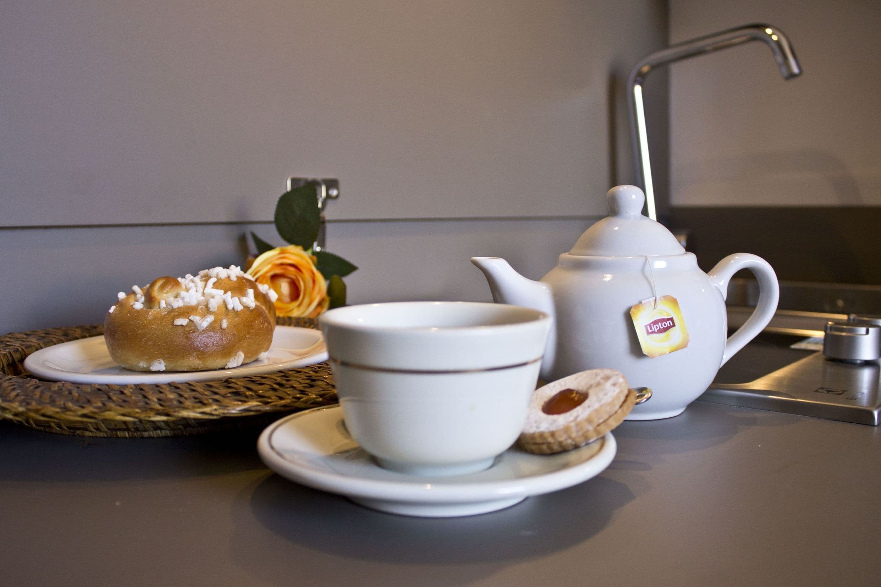 A table with a teapot, a cup, a plate with a pastry, and a decorative flower.