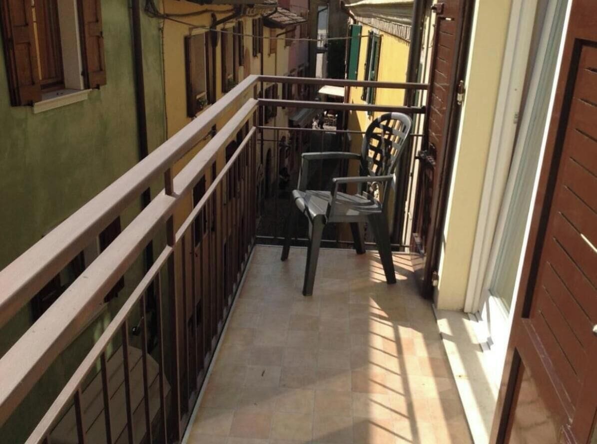 A narrow corridor with a metal railing, a chair, and a door on the right.