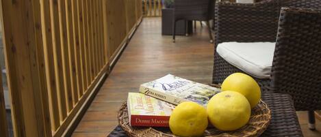 Una terraza de madera con mobiliario de mimbre y una cesta de mimbre que contiene libros y limones.